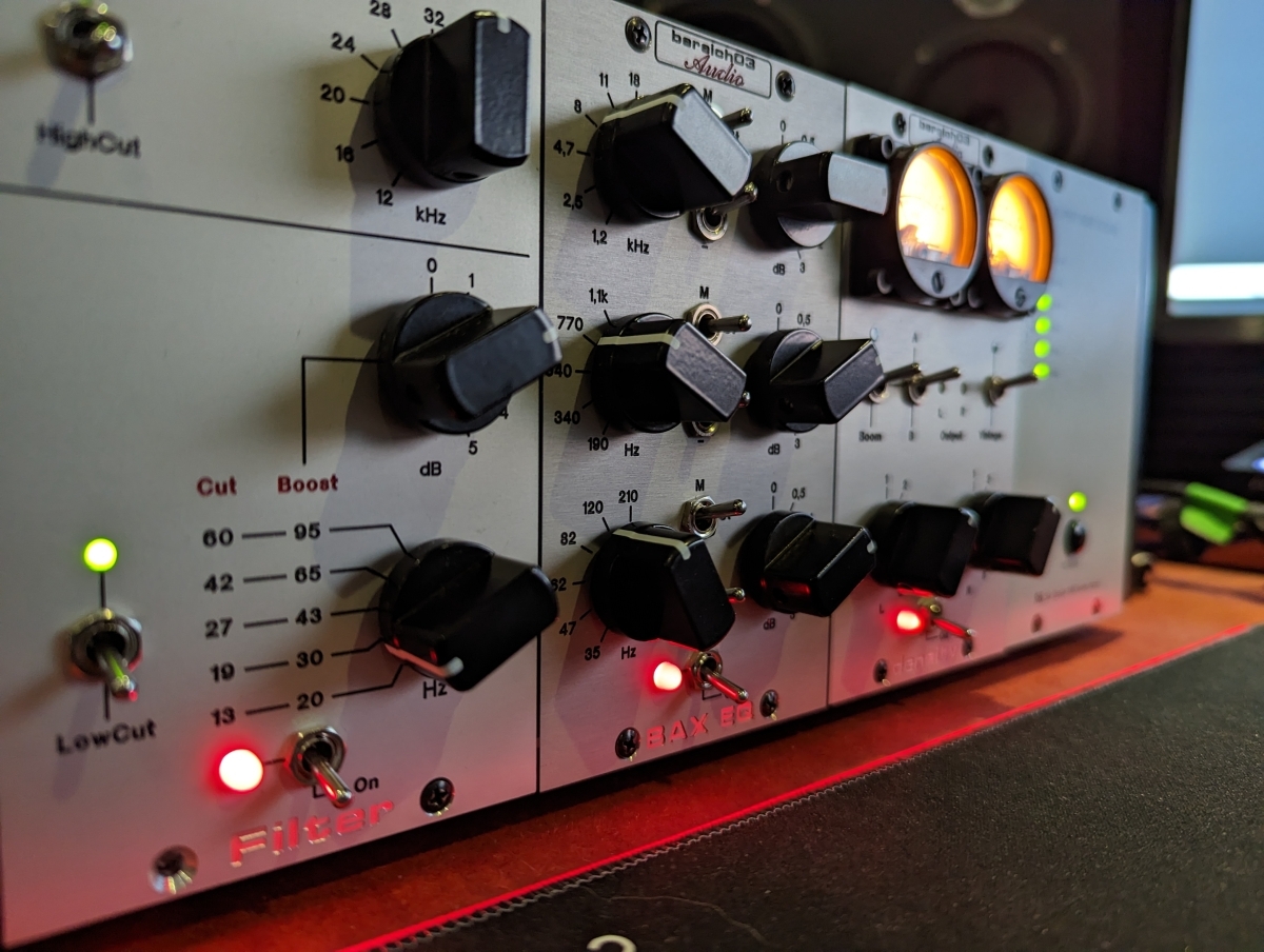 White audio mixing equipment with multiple black knobs, frequency markings, and illuminated orange/red LED indicators against dark background