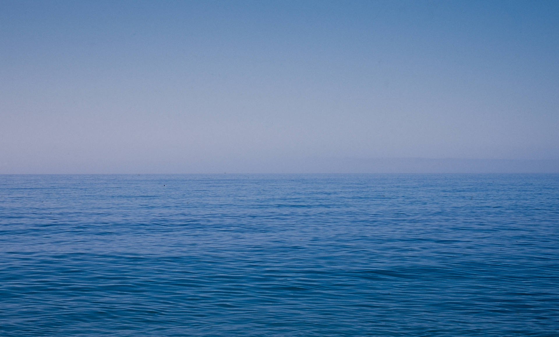 Deep blue ocean water with gentle ripples extends to horizon under clear gradient sky from pale blue to deeper blue above