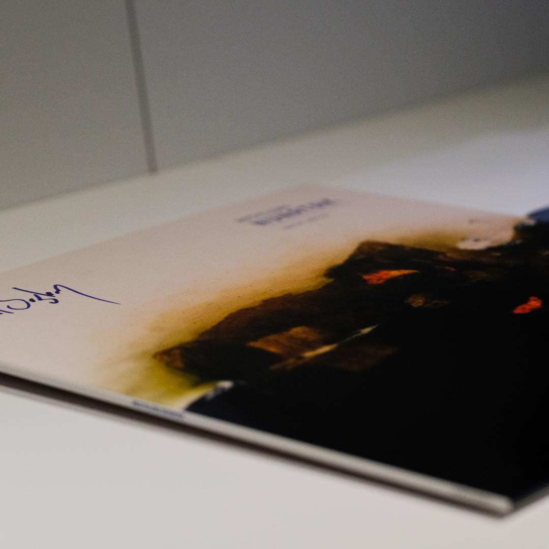 Damaged vinyl record album cover with burn marks and charred edges, showing dark artwork with orange accents and handwritten text on white background.