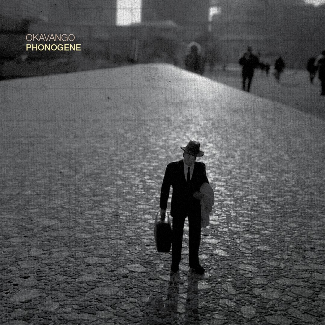 Black and white album cover showing silhouetted figure in suit and hat walking alone on cobblestone street with blurred people in background, moody atmospheric lighting.
