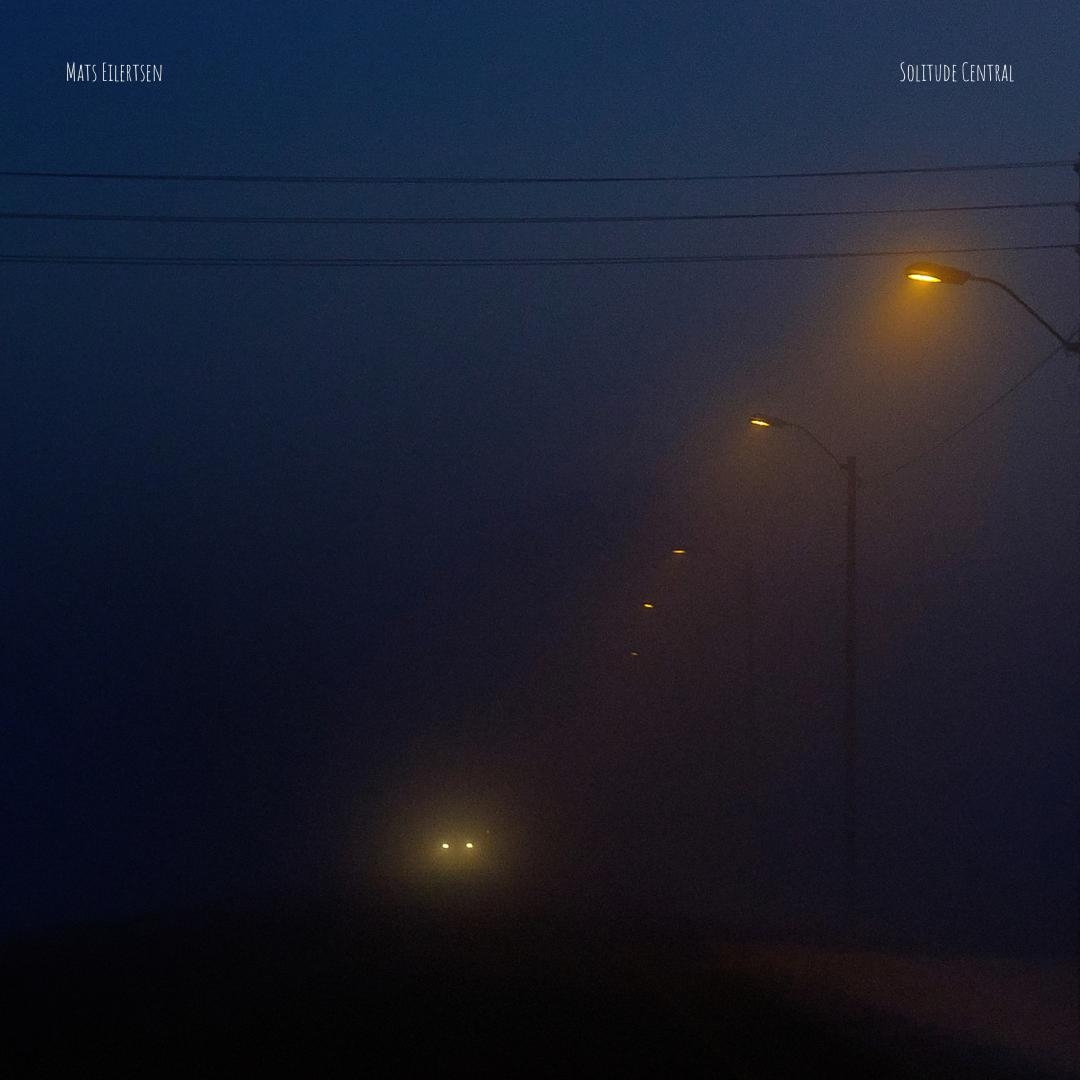 Moody blue-toned nighttime scene with glowing yellow street lamps piercing through fog, power lines crossing overhead, creating atmospheric solitude