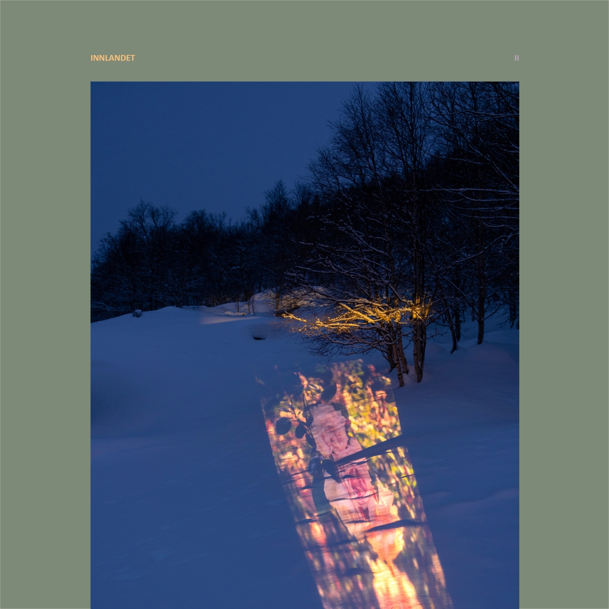 Snow-covered winter landscape at twilight with illuminated building reflected in dark water, bare trees silhouetted against deep blue sky