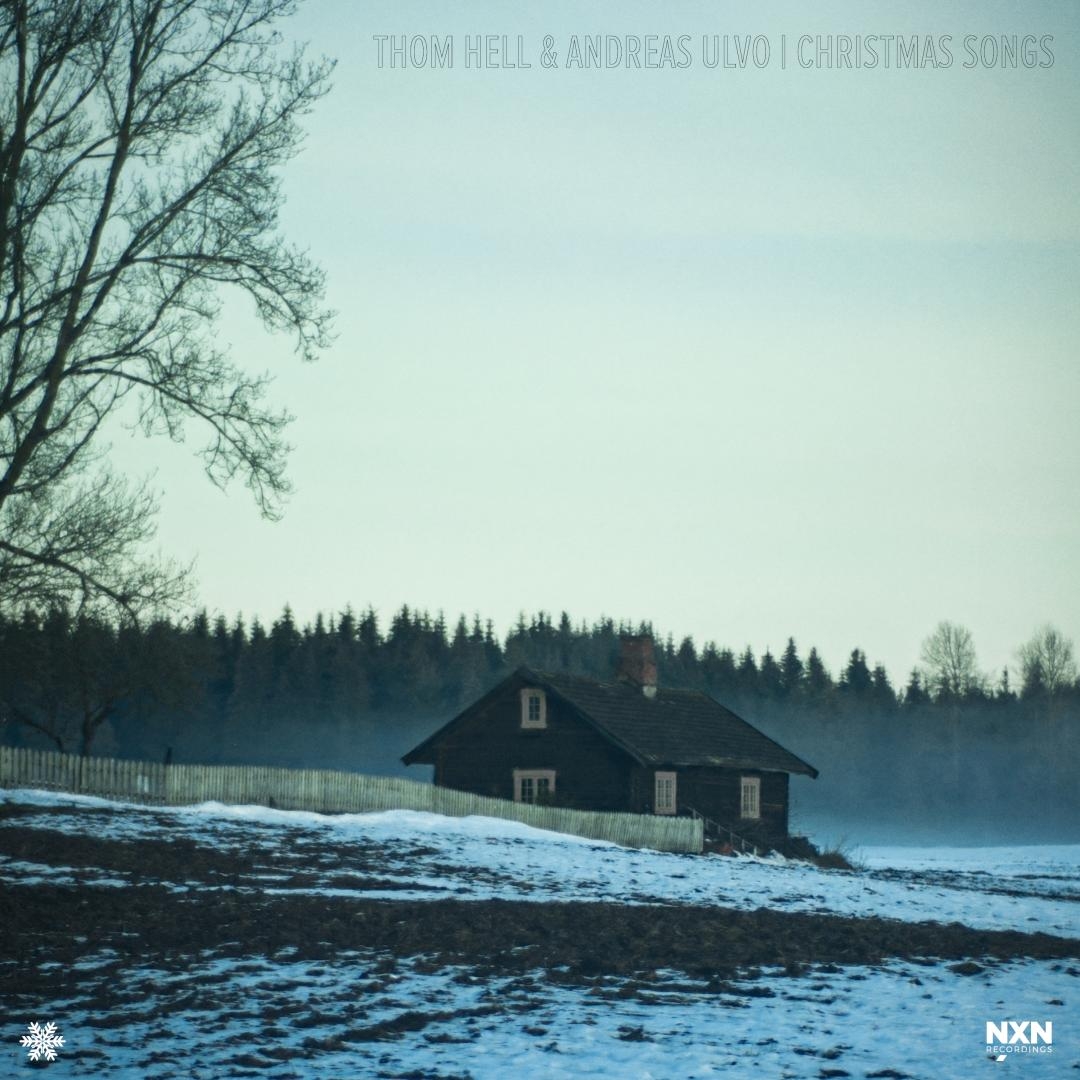 Winter landscape with snow-covered ground, dark wooden house, bare trees, evergreen forest backdrop, muted blue-green tones creating serene Christmas album artwork