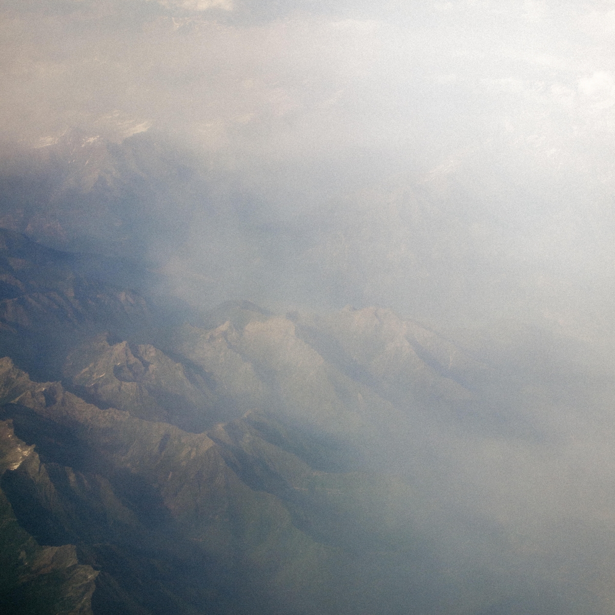 Hazy aerial view of Spanish mountains in Andalucia shrouded in soft white and blue mist, creating a dreamy, ethereal landscape with muted earth tones.