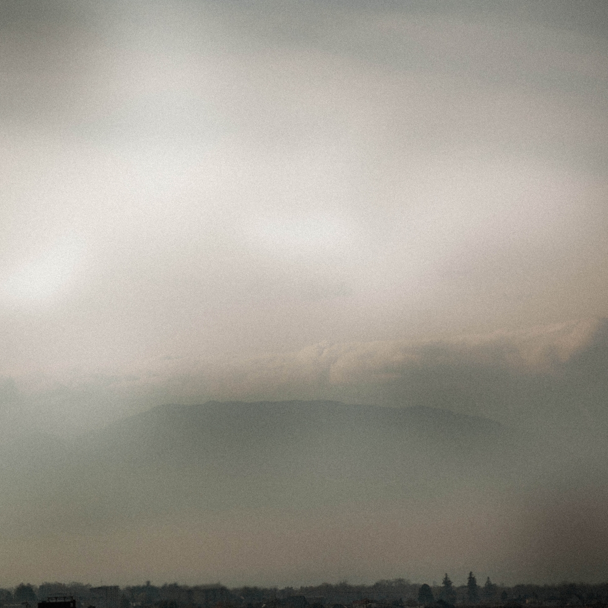 Misty gray clouds hang low over a dark treeline in rural Japan, creating a moody overcast sky with muted tones and atmospheric haze.