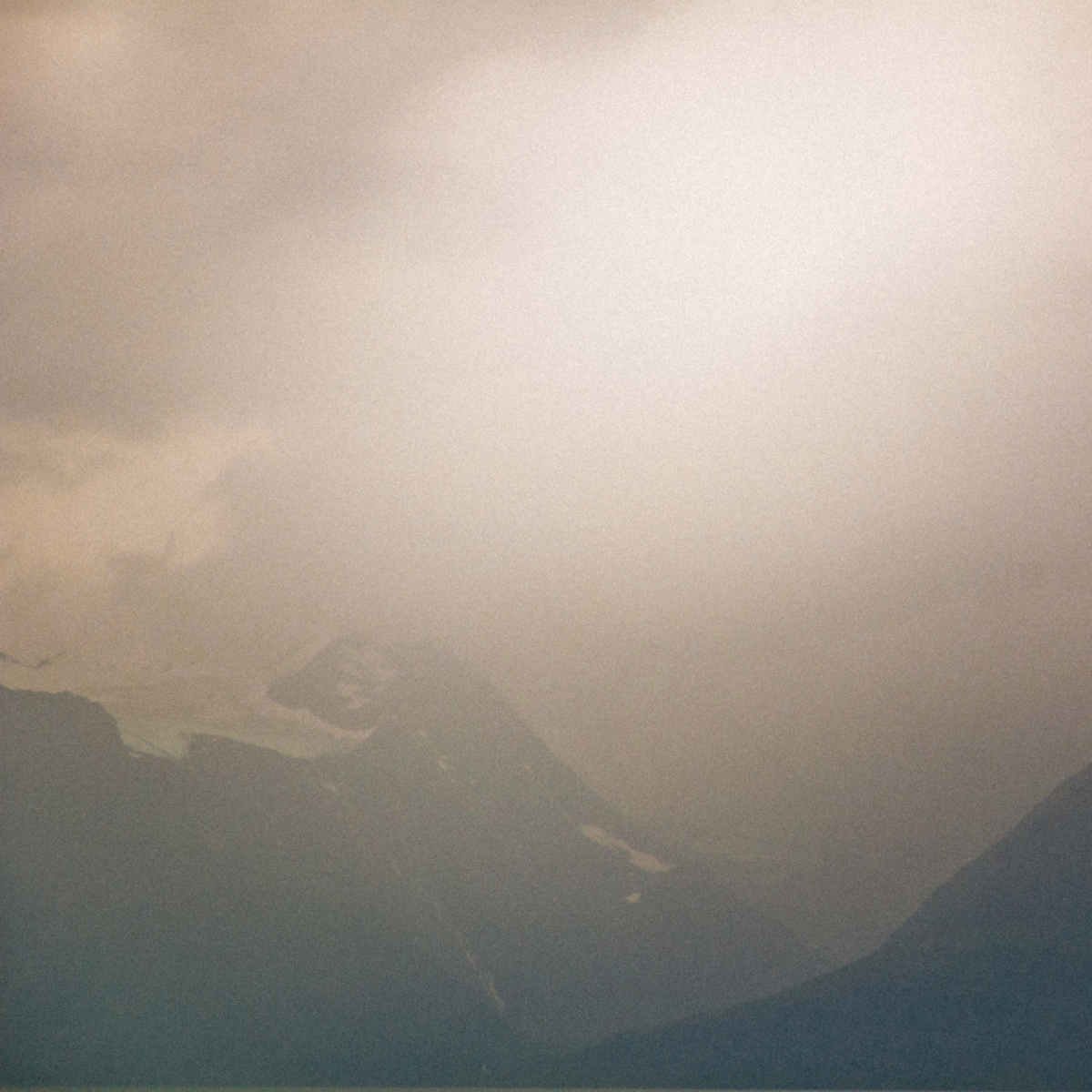 Misty mountain landscape in muted beige and gray tones with layered peaks disappearing into thick fog, creating a dreamy, ethereal atmosphere in Norway.