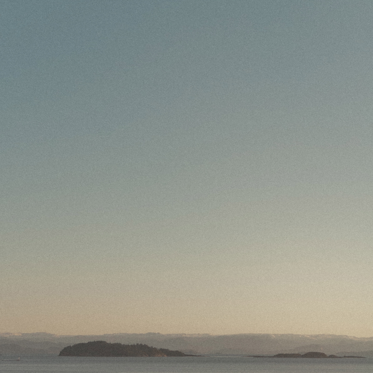 Misty seascape with silhouetted islands and rolling hills under a soft gray-blue gradient sky, creating a serene Norwegian coastal atmosphere.