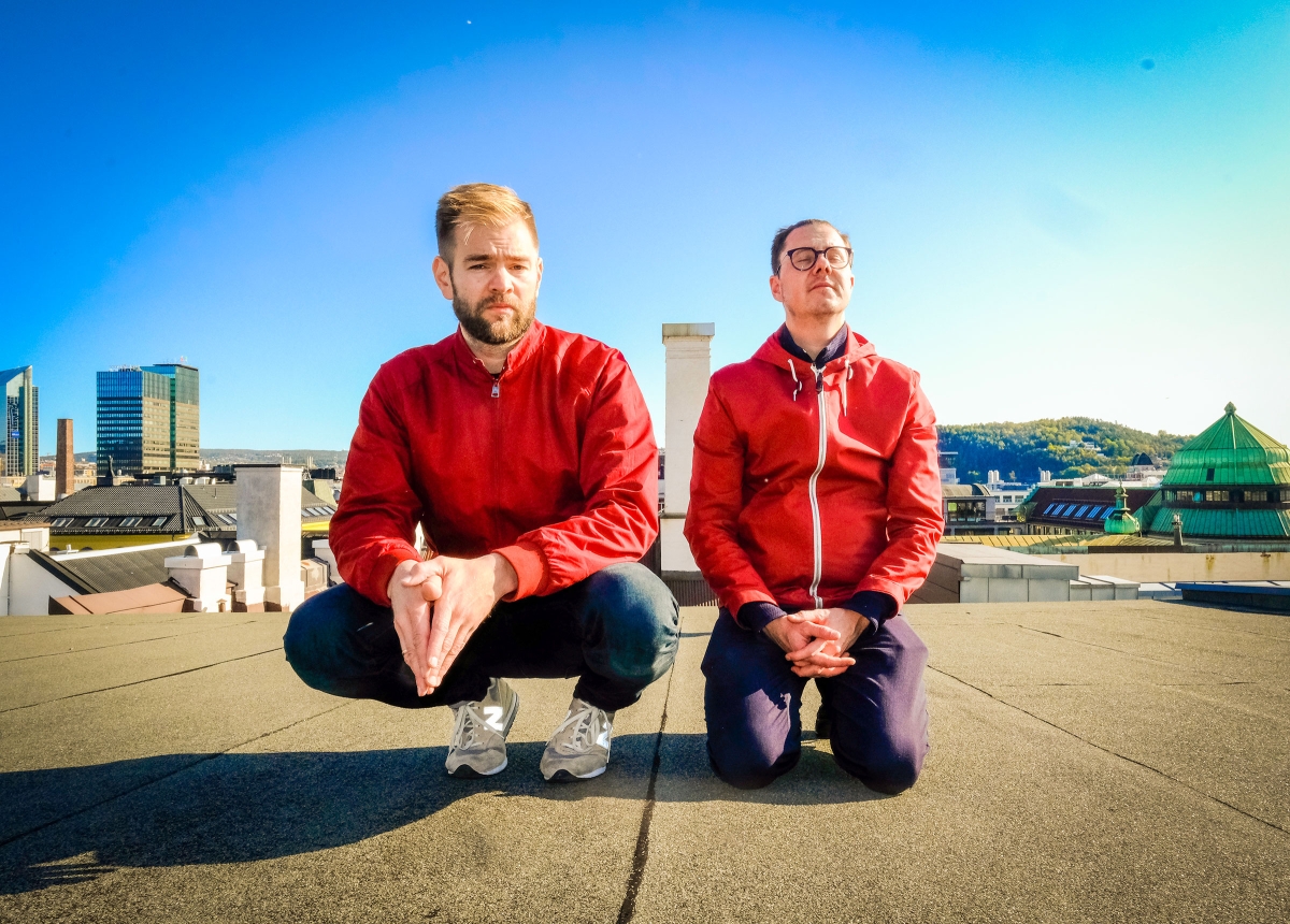 Two men on top of a roof with red jackets and blue skies. 