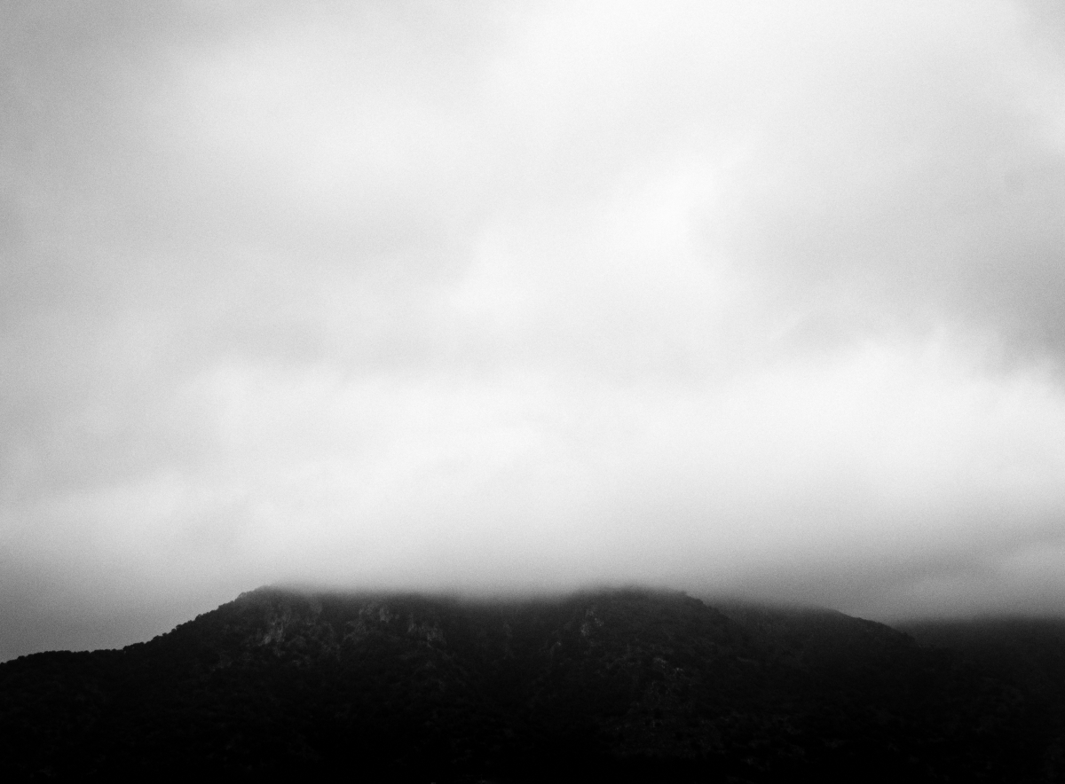 Misty mountain peak shrouded in thick gray clouds, creating a moody monochromatic landscape with dramatic atmospheric conditions.