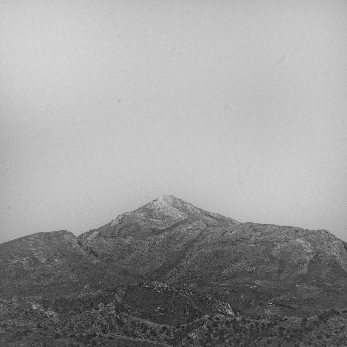 Black and white mountain landscape with layered rocky peaks under overcast sky, creating moody atmospheric composition in Nerja, Spain.