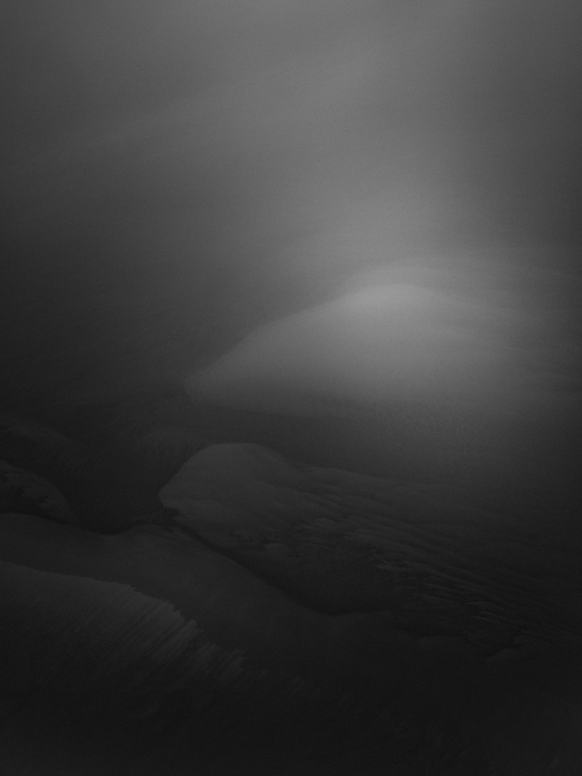 Moody black and white landscape showing misty mountains and rolling hills shrouded in dramatic fog and clouds, creating an atmospheric scene in Nice, France.