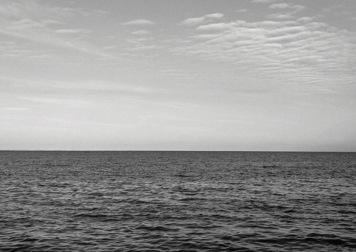 Black and white seascape showing rippled ocean waters under a cloudy sky with stratified cloud formations along the horizon