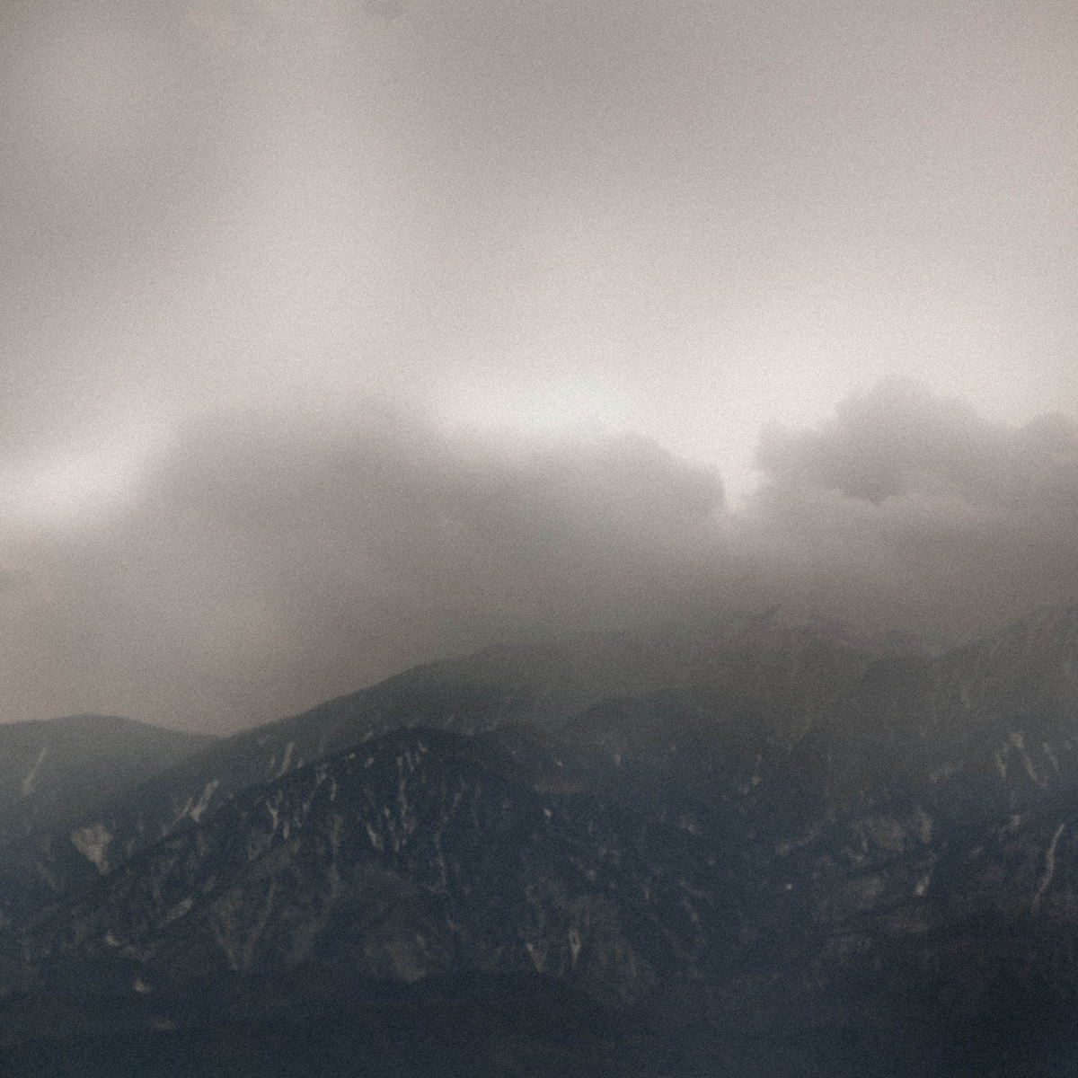 Moody mountain landscape shrouded in thick gray clouds and mist, with dark forested hills beneath an overcast Norwegian sky.