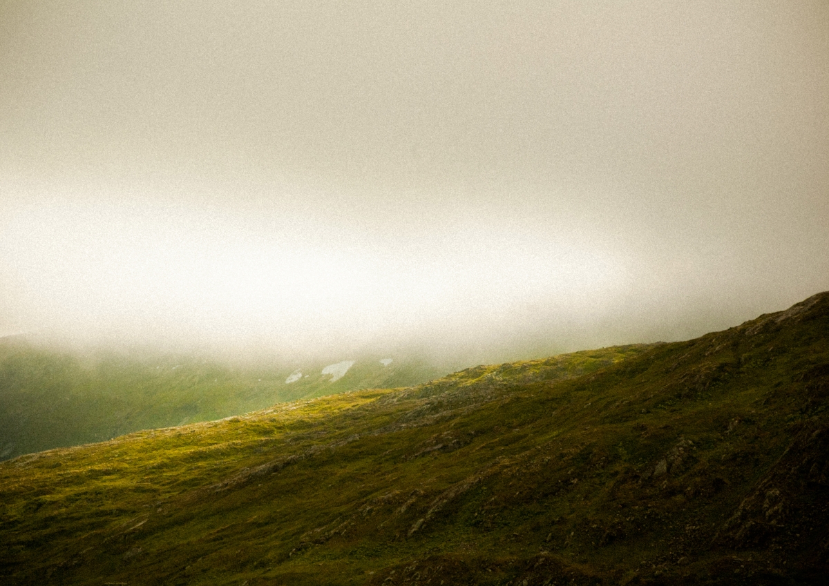 Misty mountainous landscape in Tromsø, Norway with rolling green hills disappearing into thick fog under an overcast beige sky