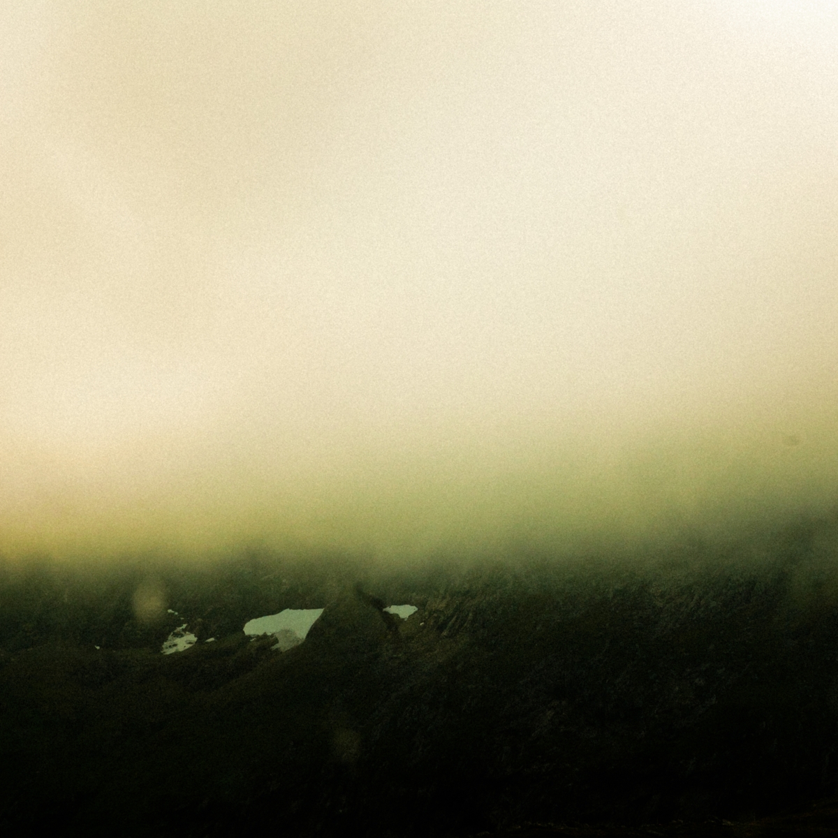 Misty mountainous landscape in Tromsø, Norway with fog rolling over dark silhouetted peaks and small pools of water, creating a moody sepia-toned atmosphere.