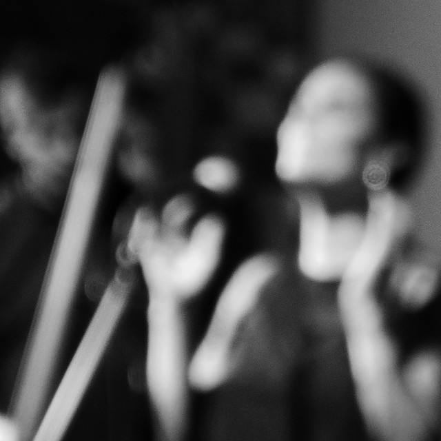 Blurred black-and-white portrait of a person tilting head back, hands raised near face, evoking emotion and motion.