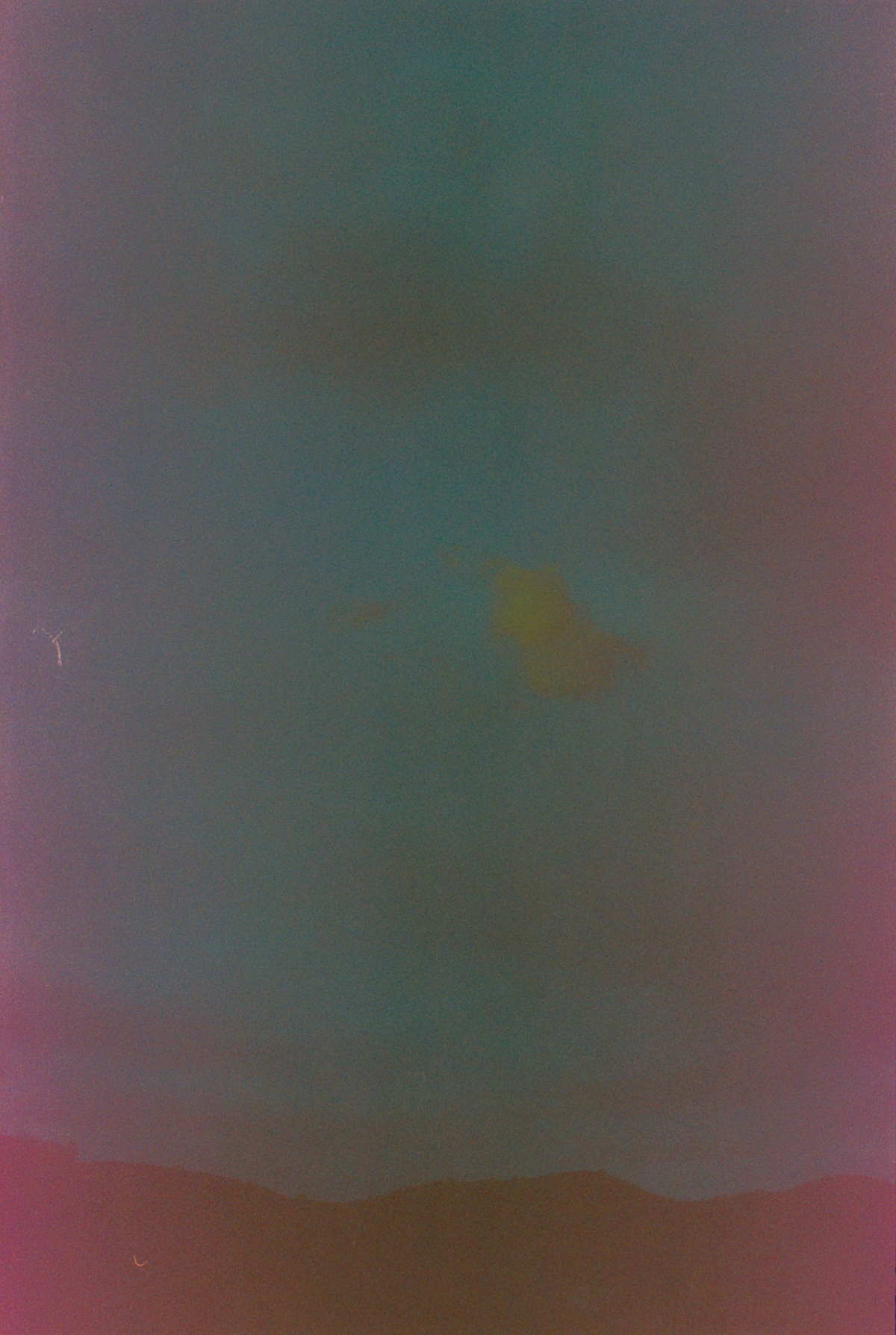 Expired film photo with heavy color shift—teal sky, magenta edges, and a yellow light leak over a dark hilly silhouette.