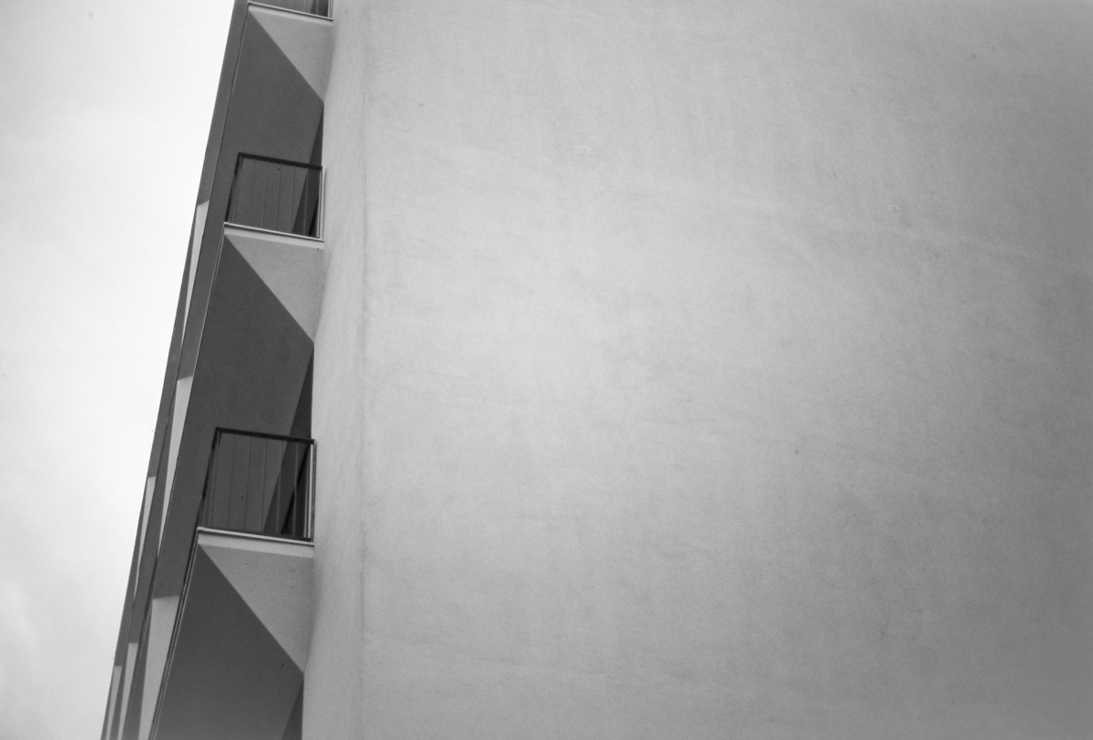 Black and white minimalist architectural shot showing corner of modern building with stacked balconies against cloudy sky