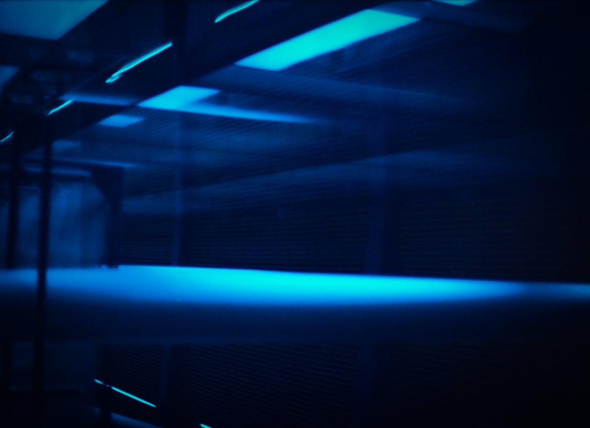 Dark industrial space with bright cyan and blue neon lighting creating dramatic streaks and reflections across empty room with concrete surfaces