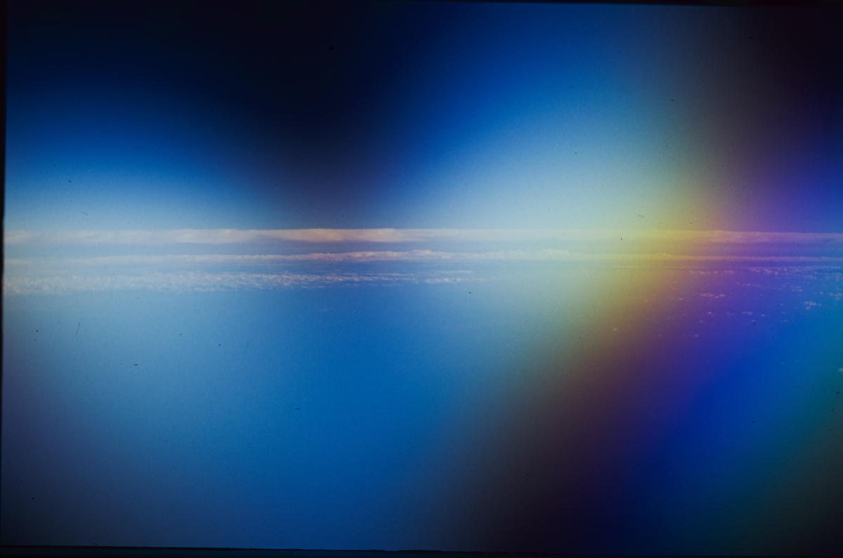 Ethereal view from space showing Earth's curved horizon with deep blue atmosphere, bright sunlight creating lens flare, and starry black space above.