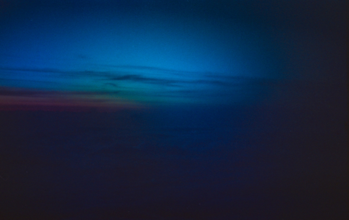 Blurred abstract seascape with deep blue ocean waters and darker blue sky, featuring subtle turquoise and reddish hues along the horizon line