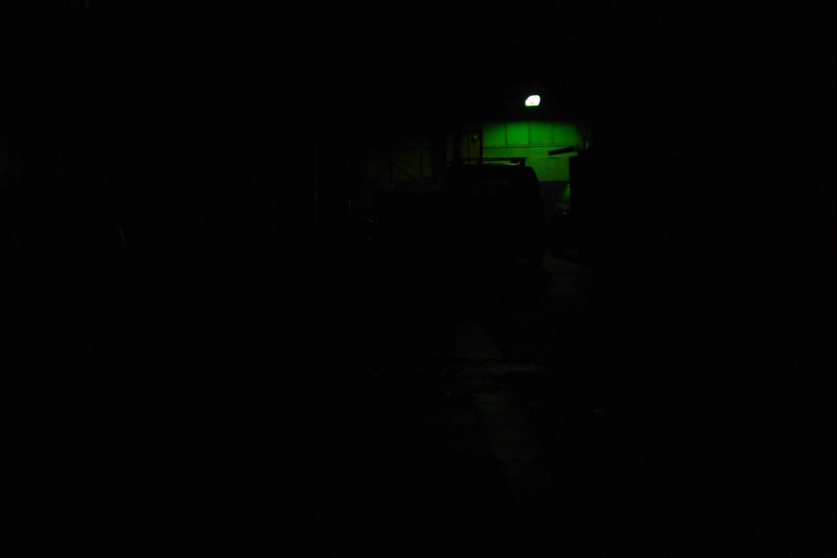 Dark nighttime scene with bright green illuminated window or screen visible in center, creating stark contrast against black surroundings