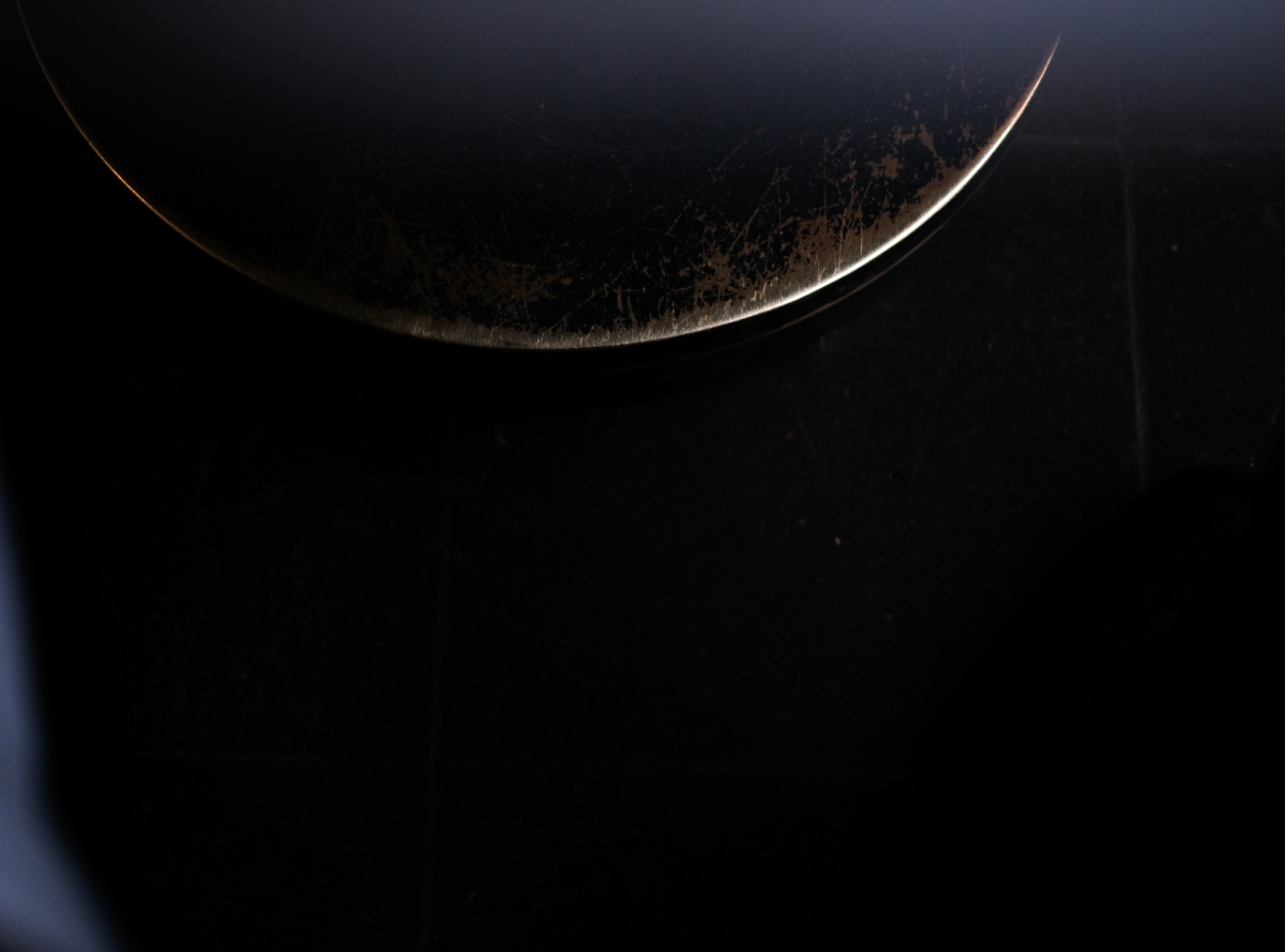 Dark atmospheric image showing curved illuminated edge of celestial body against black space, creating dramatic crescent shape with golden rim lighting