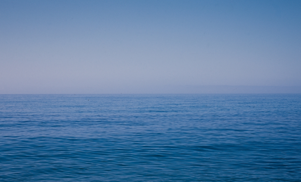 Deep blue ocean water with gentle ripples extends to horizon under clear gradient sky from pale blue to deeper blue above