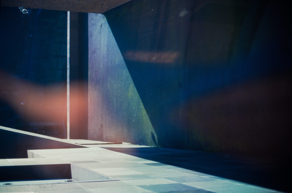 Moody architectural interior with dramatic blue lighting, concrete stairs and walls, warm orange glow in background creating atmospheric shadows