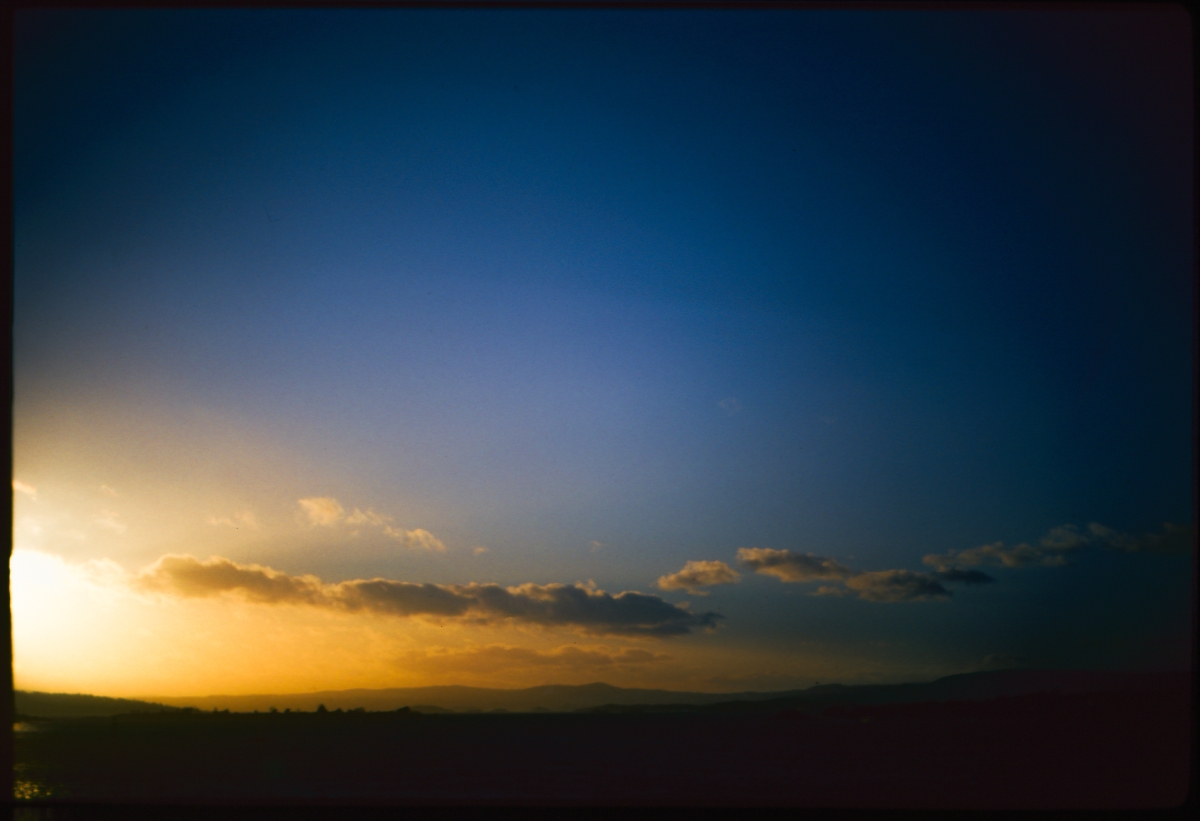 Twilight sky gradient from deep blue to golden orange at horizon, silhouetted hills below, scattered clouds catching sunset light.