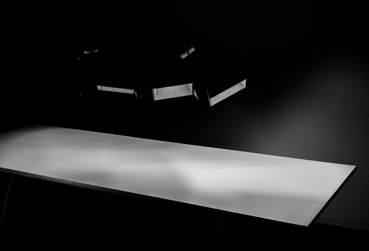 Black and white photo showing illuminated white surface under studio lights with dramatic shadows creating stark contrast and moody atmosphere