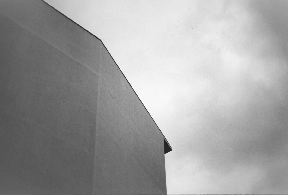 Minimalist black and white architectural detail showing curved building edge against cloudy sky, creating stark geometric contrast with moody atmosphere.