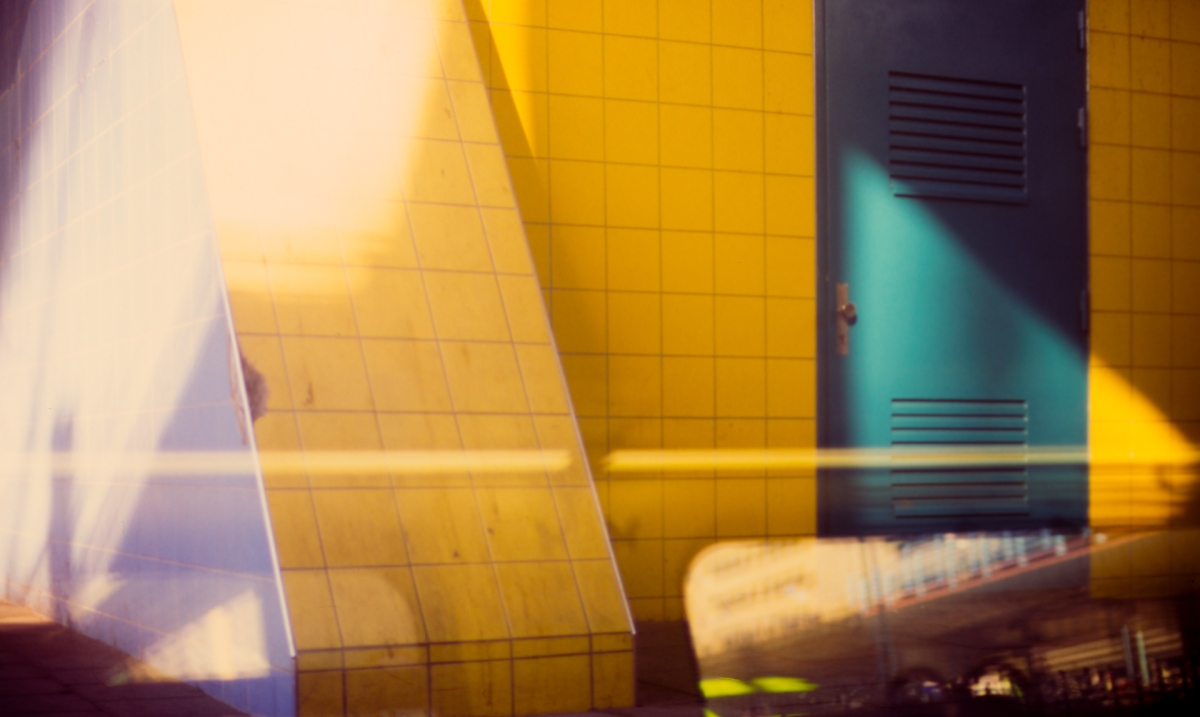 Golden yellow tiled building with curved architecture captured in motion blur, creating dynamic streaks of light and shadow with blue-green accents