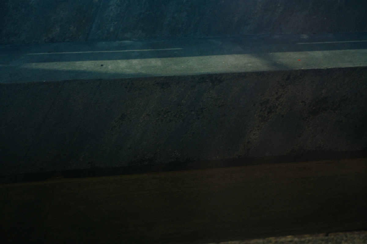 Dark moody seascape with deep teal-blue tones showing ocean waves meeting shore under dim lighting, creating atmospheric coastal scene