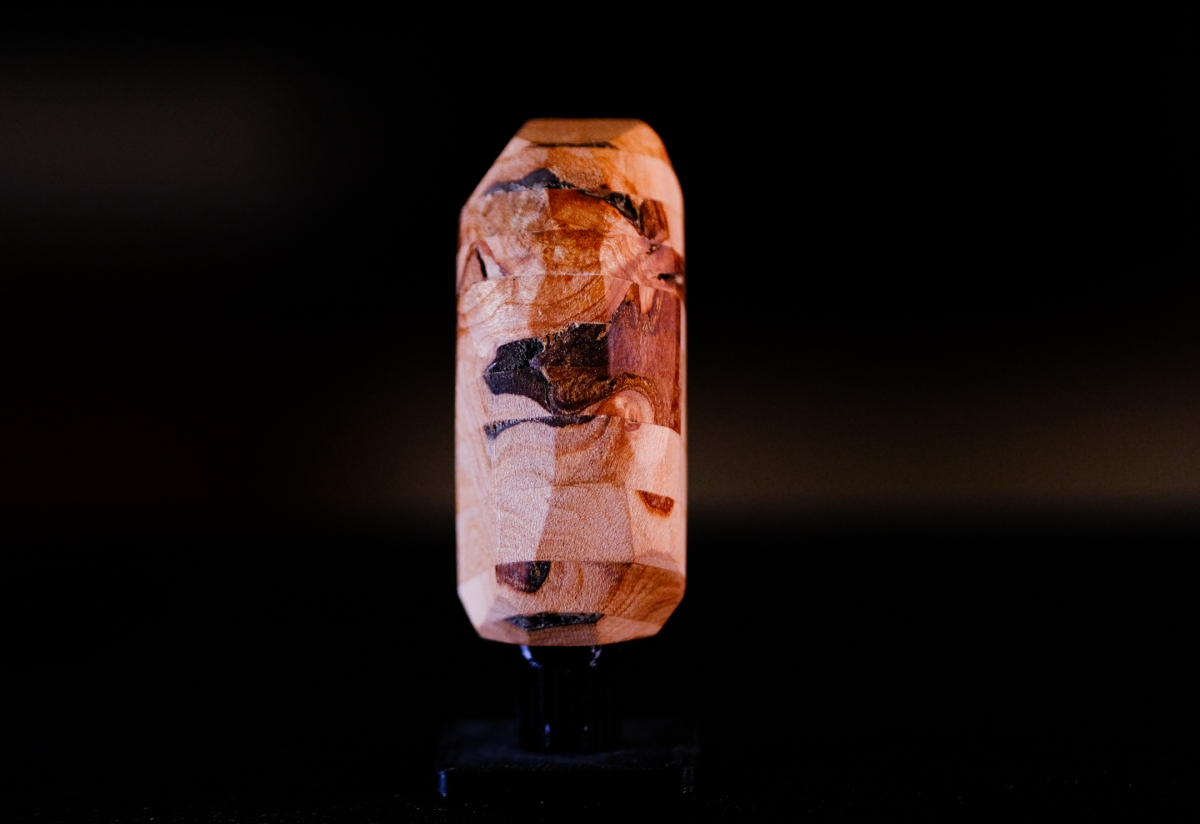 Illuminated translucent amber-colored sculptural object with dark inclusions against black background, creating warm glowing effect with orange and brown tones.