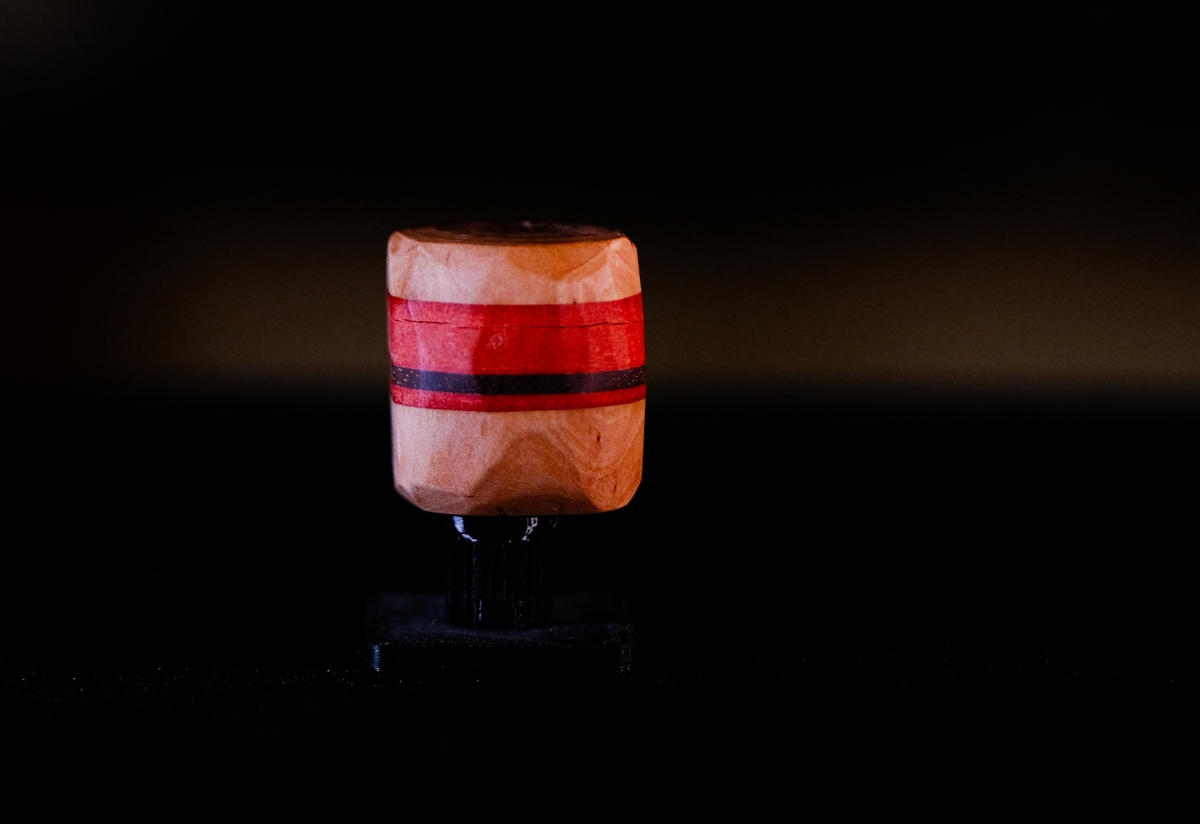 Illuminated wooden sculpture with red and black horizontal stripes against dark background, creating dramatic lighting and shadows