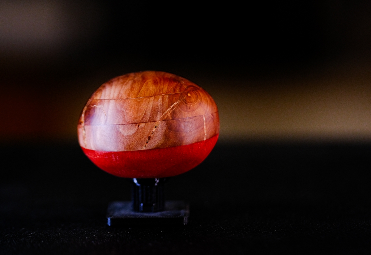 Polished red and amber oval sculpture on black stand, displaying rich translucent colors and natural crack patterns against dark background