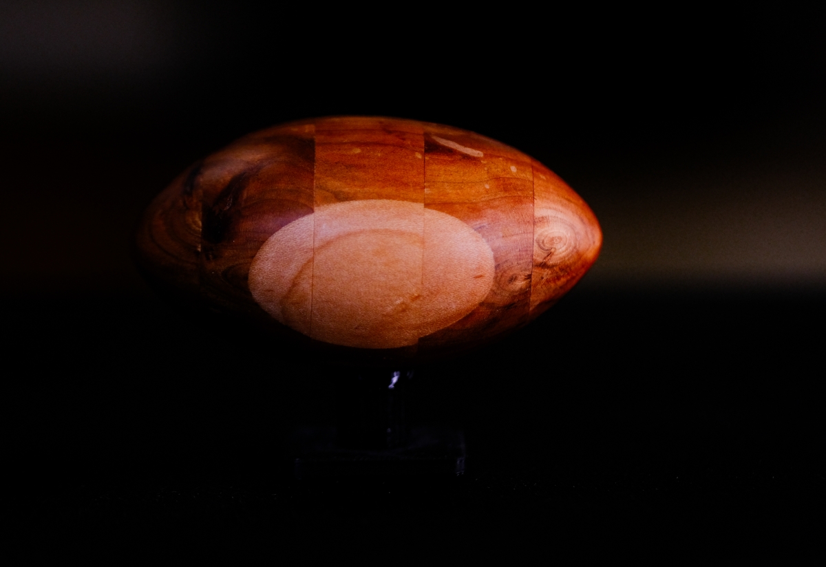 Smooth oval amber-colored sculpture with warm orange and reddish tones, illuminated against a dark background, creating an ethereal glowing effect.