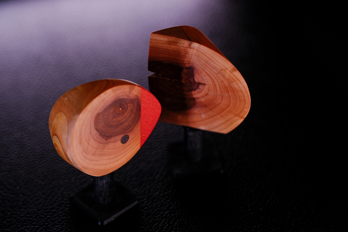 Two wooden bowl sculptures with rich grain patterns on black pedestals, one featuring red accent coloring, displayed against purple-tinted background