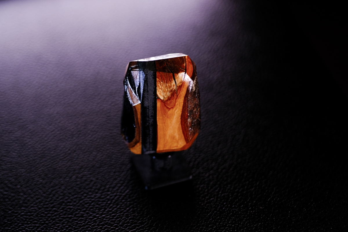 Faceted amber and black crystal sculpture with geometric cuts reflecting warm orange and golden light against dark textured surface