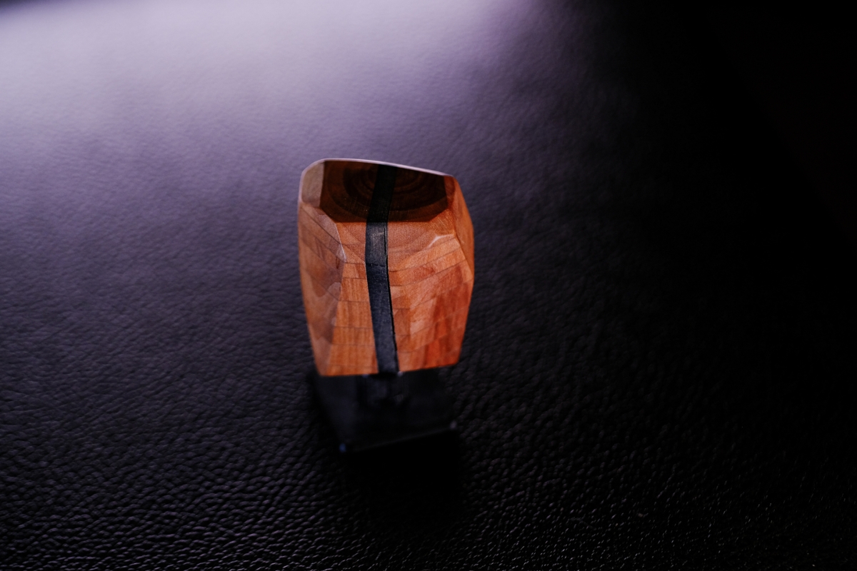 Handcrafted wooden ring with rich orange wood grain and black inlay stripe, photographed on dark textured surface with dramatic lighting