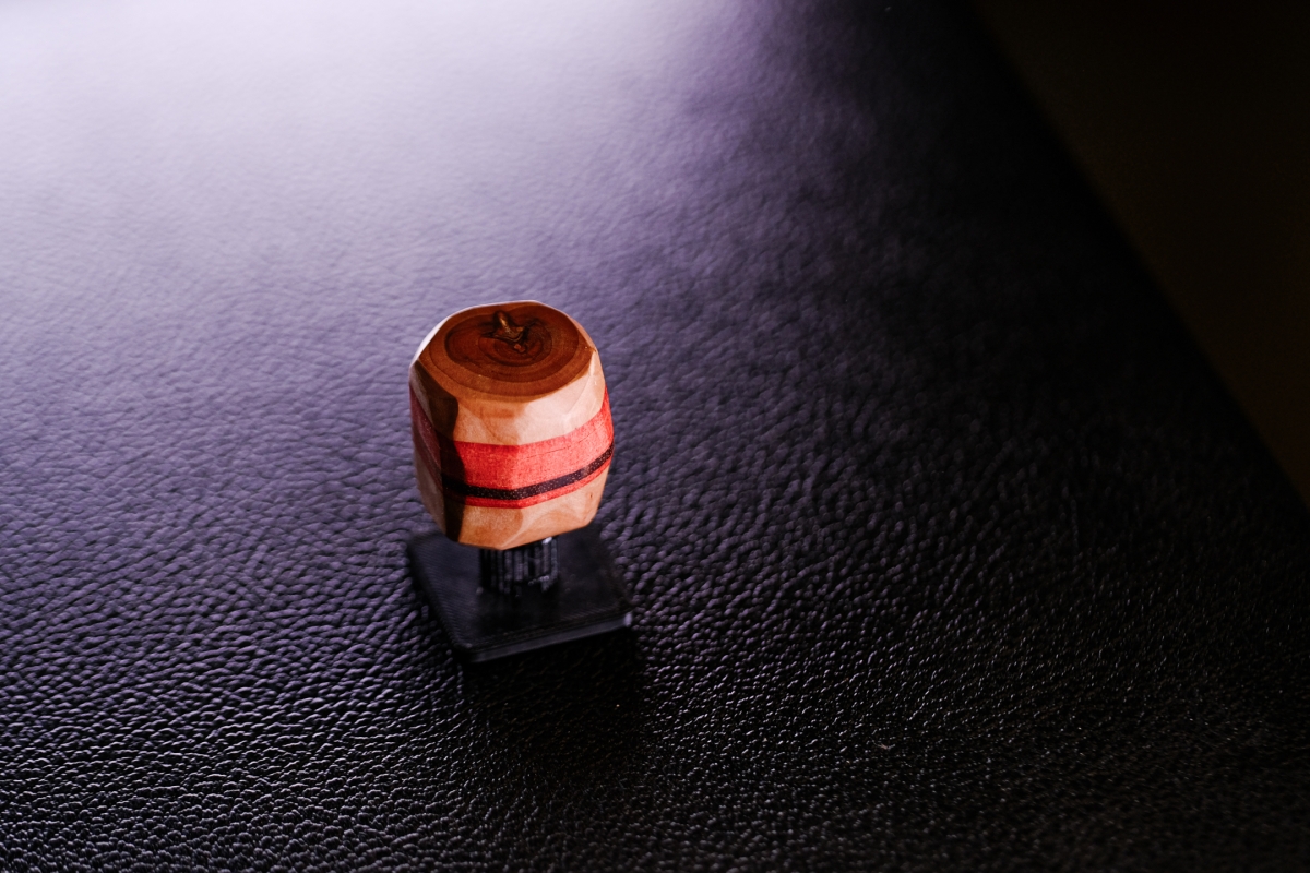 Wooden rubber stamp with red and pink stripes on black textured surface, dramatic lighting creates purple-tinted shadows and highlights