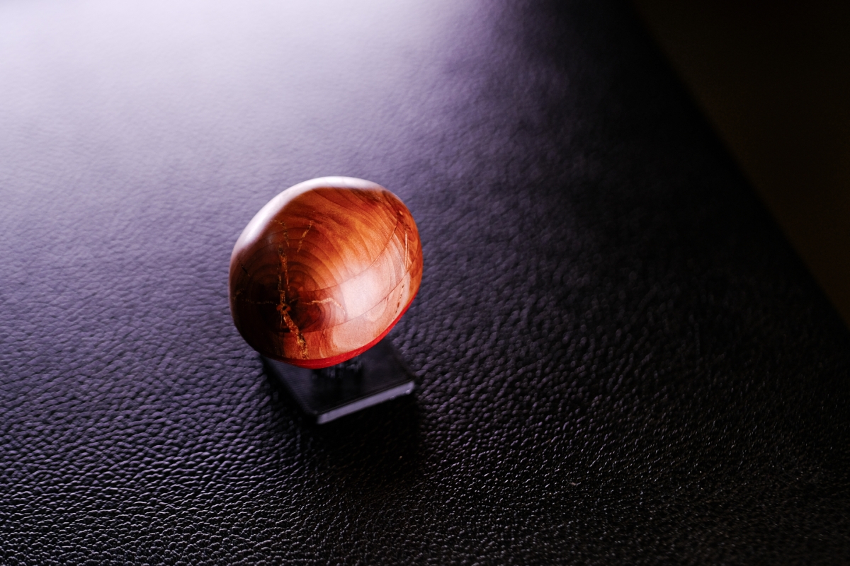 Polished red-brown wooden egg sculpture on dark textured surface with dramatic purple-tinted lighting creating artistic shadows and highlights