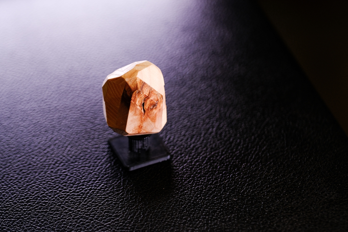 Orange geometric crystal sculpture casting shadow on textured black surface with dramatic lighting creating moody atmosphere