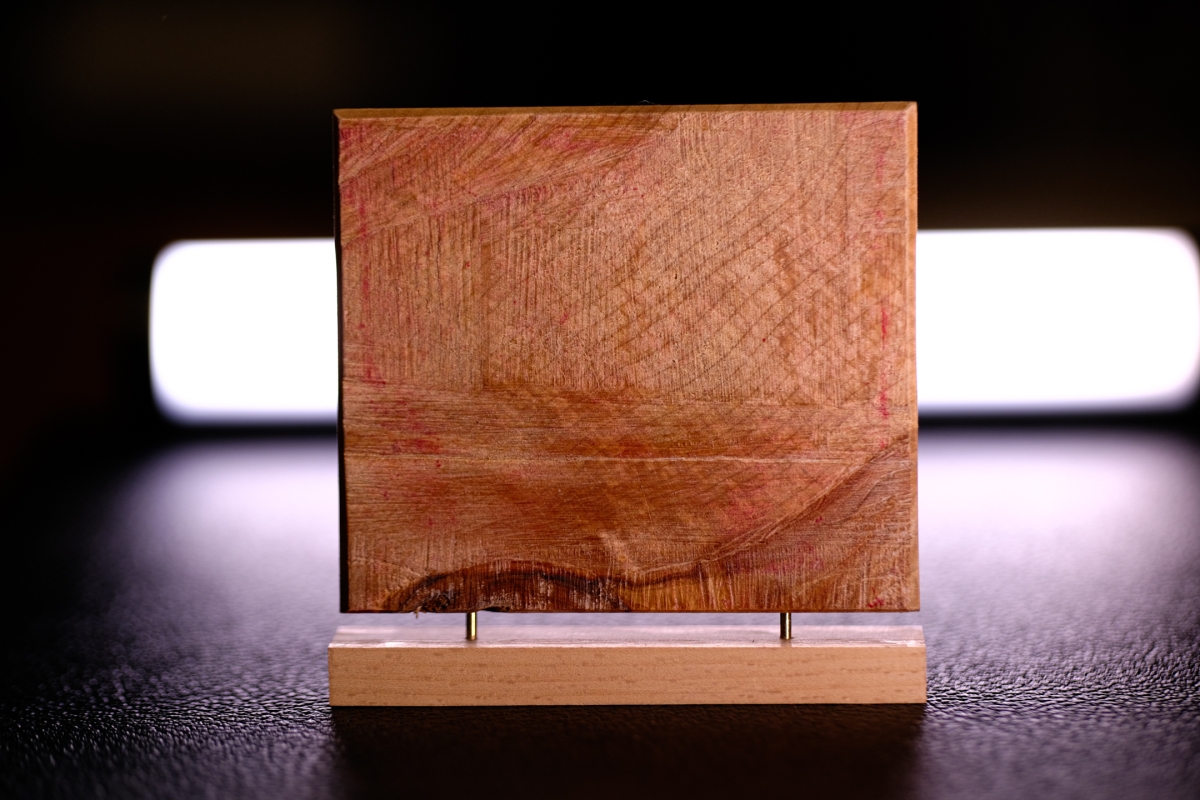 Wooden sculpture with intricate carved patterns displayed on light wooden base against dark background with soft white lighting behind