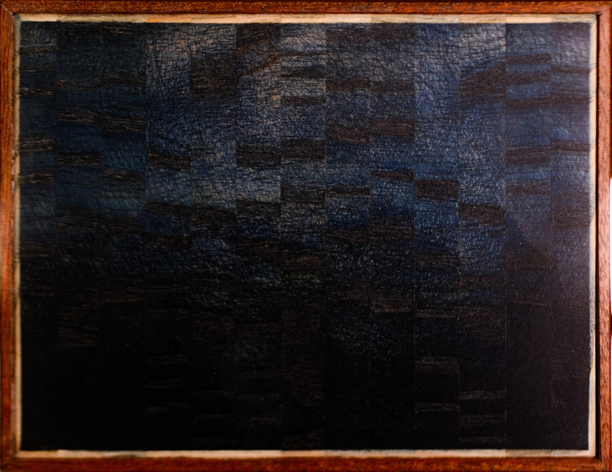 Framed abstract artwork with dark blue and black brushstrokes in wooden frame, sitting on textured surface with soft lighting in background.