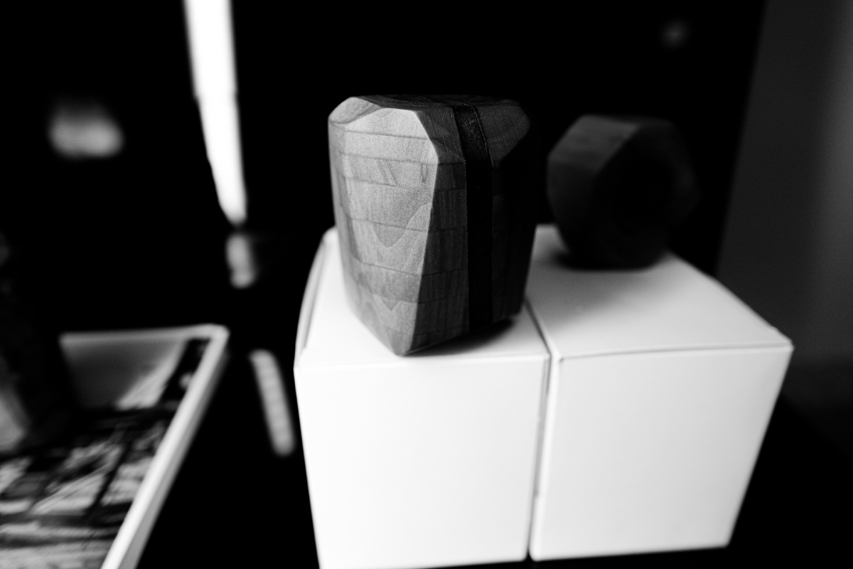 Black and white photo showing geometric wooden sculptures stacked on white blocks, with soft lighting creating dramatic shadows and depth