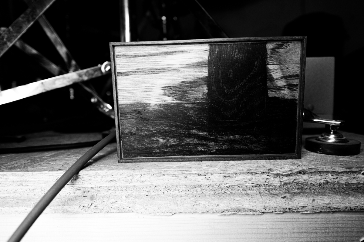 Black and white photo showing a framed drawing of a sailboat on water, positioned on weathered wooden surface with nautical equipment in background