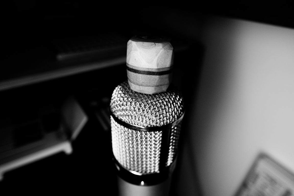 Black and white close-up of vintage ribbon microphone with mesh grille and cylindrical body, artistic lighting creates dramatic shadows