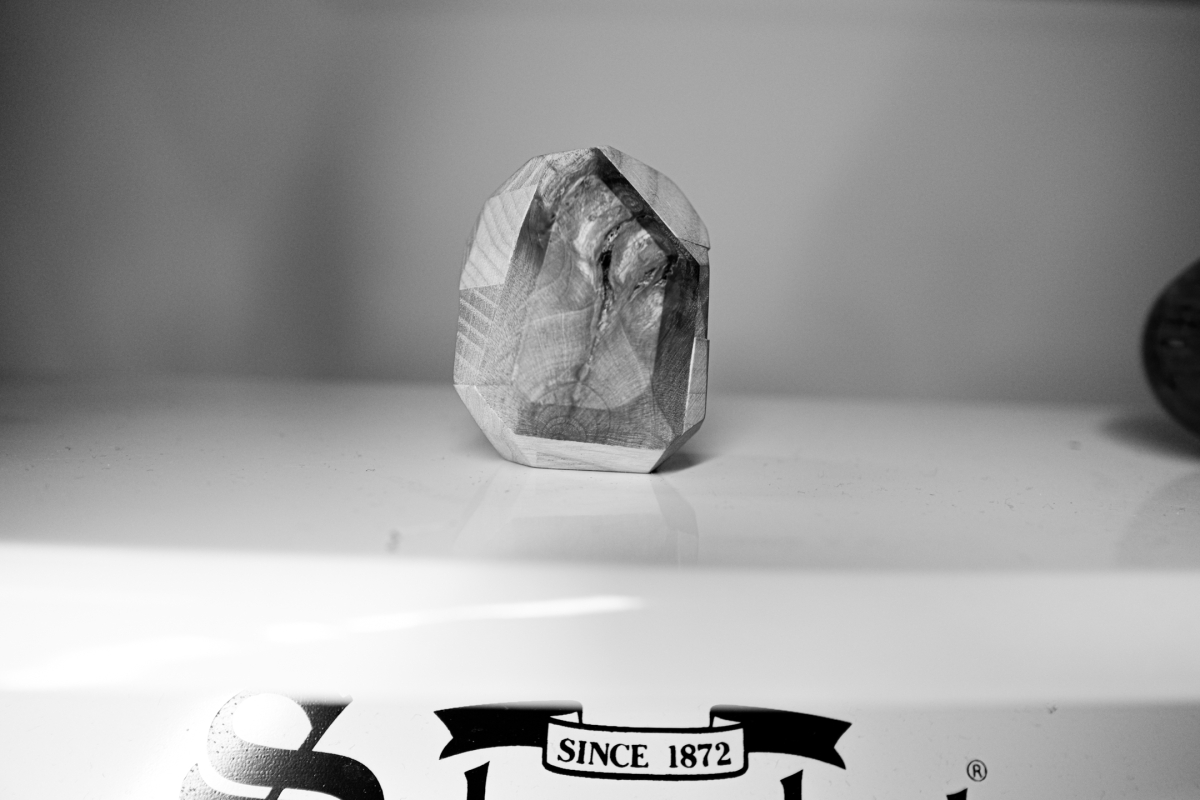 Black and white photo showing a faceted crystal or geometric glass sculpture sitting on a white surface with "SINCE 1872" text visible below